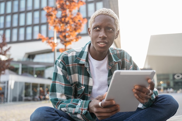 Estudante afro-americano bonito usando tablet digital estudando aprendizagem de idiomas sentado no campus