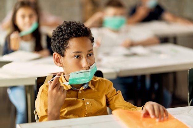 Estudante afro-americano colocando máscara facial protetora na sala de aula