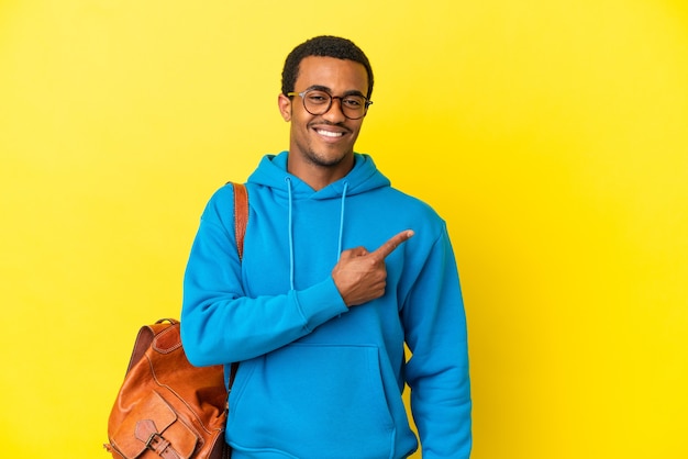 Estudante afro-americano sobre fundo amarelo isolado apontando para o lado para apresentar um produto