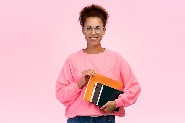 Estudante afro-americano sorridente em óculos segurando livros isolados no fundo. Educação