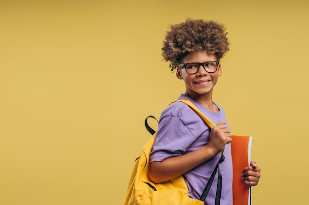 Estudante afro-americano sorridente segurando mochila e livros usando óculos elegantes