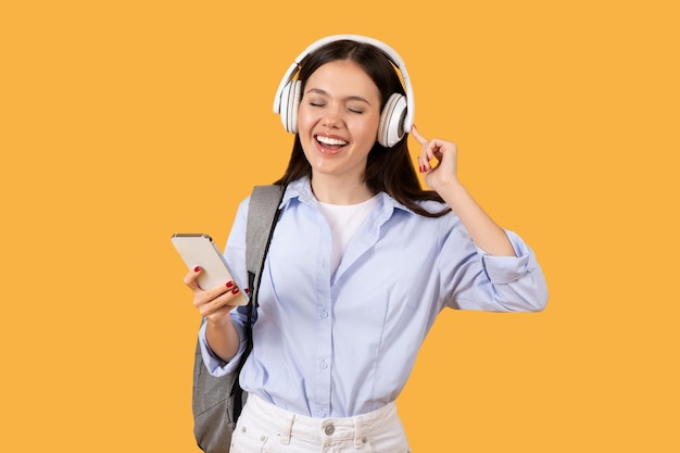 Estudante alegre com telefone e fones de ouvido em fundo amarelo