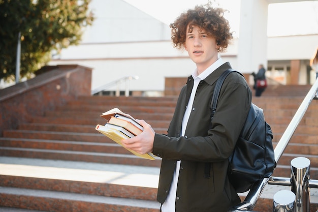 Estudante animado tendo intervalo entre as aulas perto da universidade sorrindo para a câmera ao ar livre