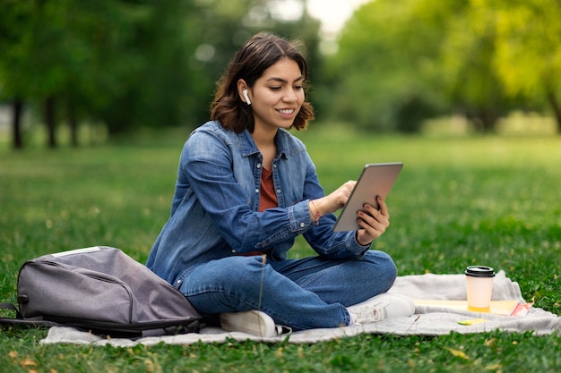 Estudante árabe sorridente navegando na Internet no tablet digital enquanto relaxa ao ar livre