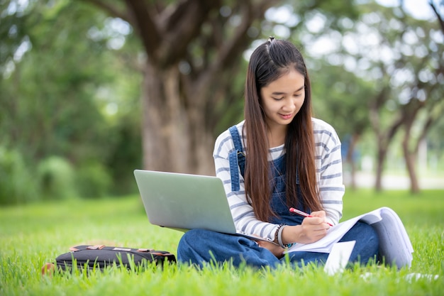 Estudante asiática bonita que guarda livros e sorrindo e aprendizagem e educação no parque no verão para relaxar o tempo