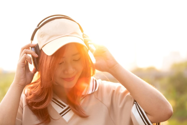 Foto estudante asiática feliz gosta de ouvir música com fone de ouvido depois da aula no parque natural da cidade