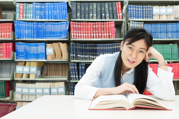 Estudante asiática lendo livro na biblioteca