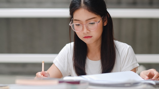 Estudante asiática lendo livros na biblioteca da universidade