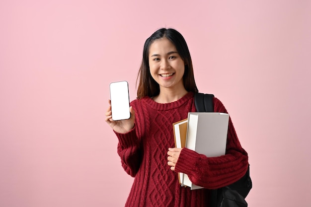 Estudante asiática sorridente, mostrando um modelo de tela branca do smartphone, um fundo rosa