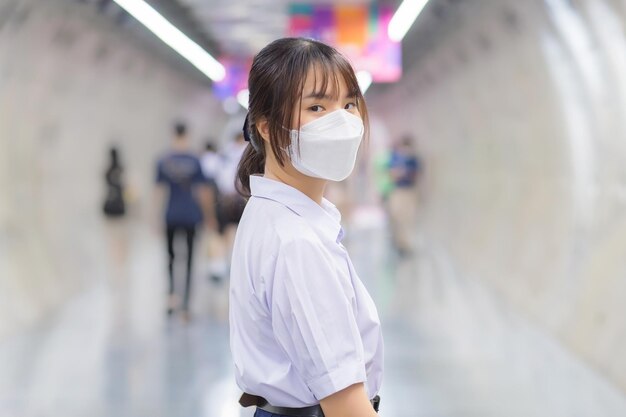 Estudante asiático de uniforme está andando em um túnel subterrâneo para pegar o metrô para a escola de manhã