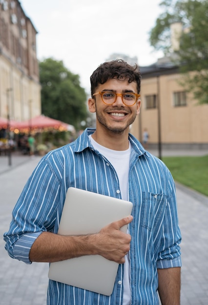 Estudante asiático sorridente segurando laptop olhando para câmera no campus universitário Conceito de educação