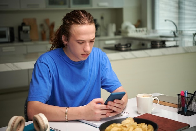 Estudante bebendo café da manhã e verificando mídias sociais no smartphone