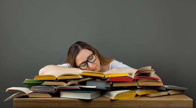 Estudante cansada com óculos dormindo em livros na biblioteca