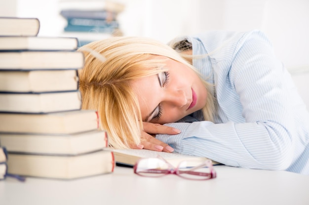 Estudante cansado caiu um sono entre muitos livros, enquanto aprende.