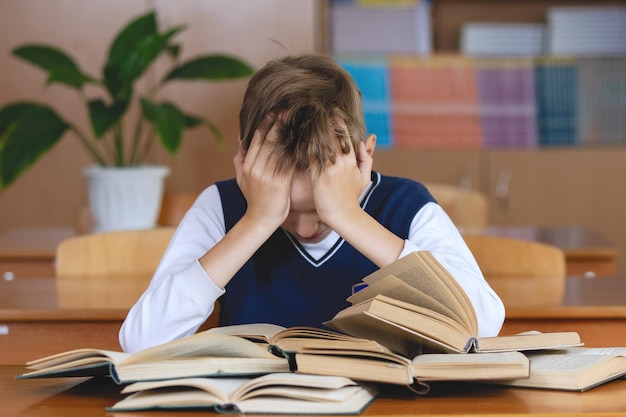 Estudante cansado dorme em sua mesa, em uma pilha de livros.