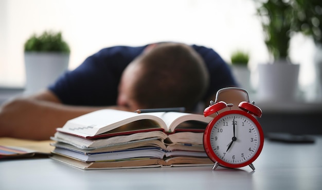 Estudante cansado no local de trabalho no quarto tomando uma sesta em uma pilha de livros didáticos Homem adormecido descansando durante a educação depois de uma noite sem dormir Estudante em desespero causado pelo conceito de prazo de exame