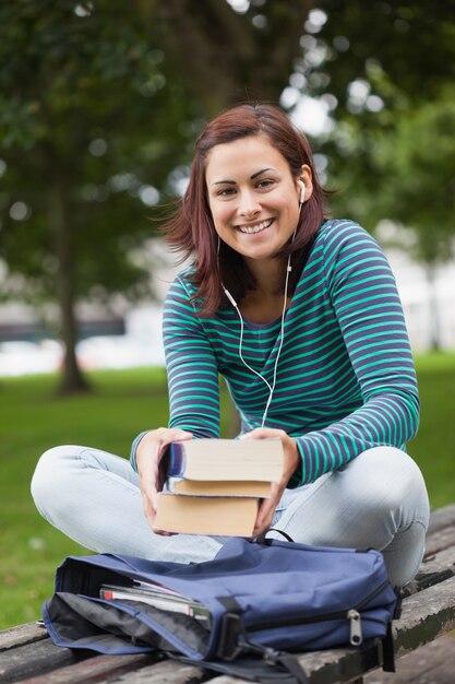 Foto estudante casual alegre sentado em livros de banco segurando