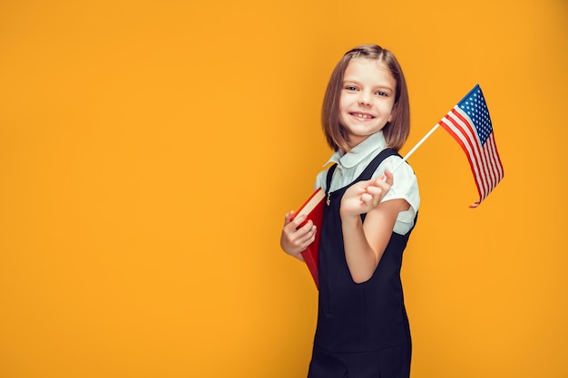 Estudante caucasiana sorridente segurando a bandeira americana e um livro nas mãos sobre a bandeira dos eua de fundo amarelo