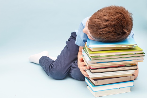 Estudante chateado sentado com uma pilha de livros escolares Menino dormindo sobre uma pilha de livros didáticos