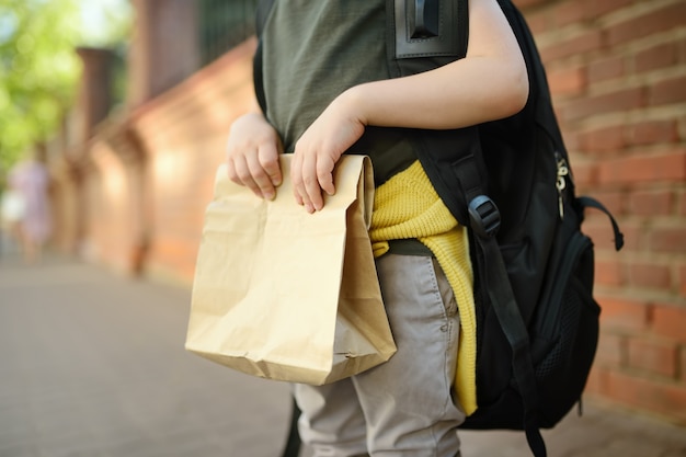 Estudante com mochila grande e lancheira perto do prédio da escola.