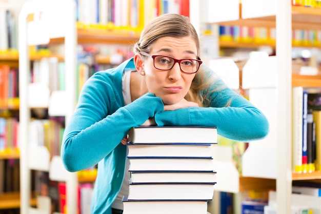 Estudante com pilha de livros aprendendo na biblioteca