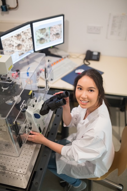Estudante de bioquímica usando grande microscópio e computador