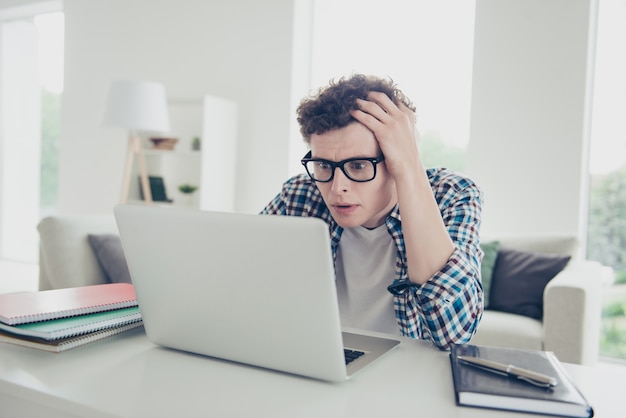 Estudante de cara bonito vestindo uma camisa xadrez casual olhando para o laptop