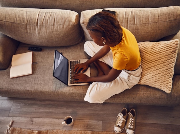 Estudante de ensino à distância escrevendo estudando e digitando em um laptop fazendo um teste de atribuição virtual no sofá em casa Vista acima de uma jovem escritora ou editora de idiomas digitando um ensaio on-line