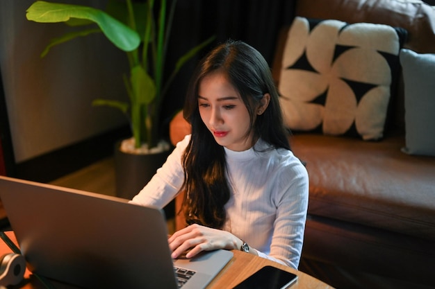 Estudante de faculdade asiática concentrada ou freelancer trabalhando em seu projeto no laptop