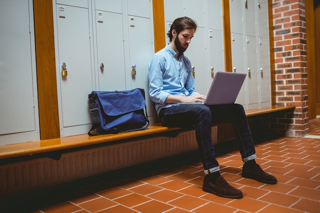 Estudante de Hipster usando o laptop no corredor