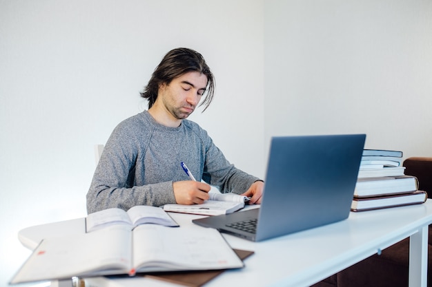 Estudante de homem escrever no caderno trabalhando no computador. marketing na internet, trabalho freelance, trabalhar em casa, aprendizagem online, estudar, conceito de bloqueio. educação a distância, livros sobre a mesa