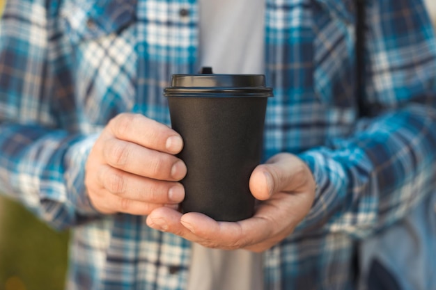 Estudante de homem segurando na mão uma xícara de café de papel preto para viagem