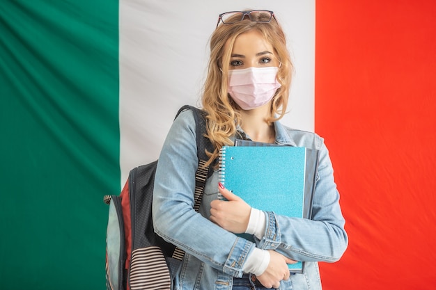 Estudante de italiano segura livro didático, usa mochila e máscara facial.