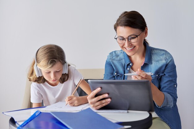 Estudante de mãe e filha aprendendo lições escolares juntos em casa pai ajudando criança usando aulas de tablet digital na Internet garota em fones de ouvido escreve no caderno com lápis