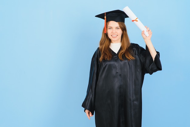 Estudante de pós-graduação, mulher, usando vestido e chapéu de formatura, sobre fundo azul