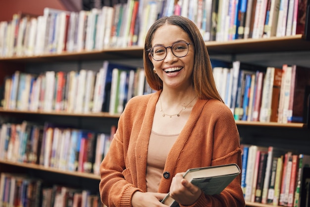 Foto estudante de rosto e mulher na universidade na biblioteca pronta para aprender educação de retrato e mulher feliz do brasil parada na estante com livro para estudar conhecimento e pesquisa de literatura