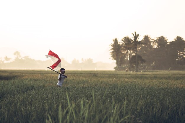 Estudante do ensino fundamental indonésio agitando bandeira indonésia com espírito no campo de arroz.