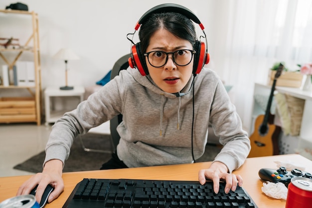 Estudante do ensino médio nerd jovem jogando jogo de computador em fones de ouvido. competição online de gamer geek feminino asiático fique em casa nas férias de verão e não vá ao ar livre. garota da faculdade estilo de vida junk food lanche