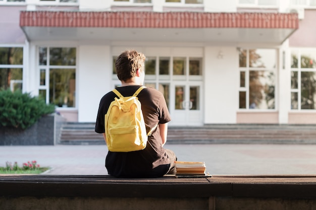 Estudante do primeiro ano sentado fora de uma universidade ou escola. calouro esperando o inicio das aulas