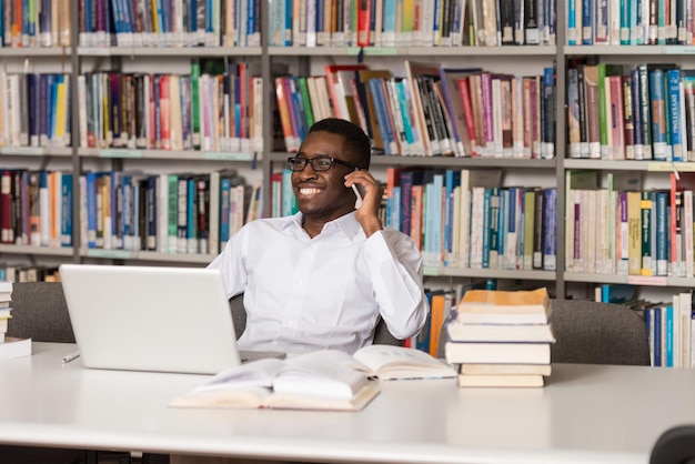 Estudante do sexo masculino africano falando ao telefone na biblioteca rasa profundidade de campo