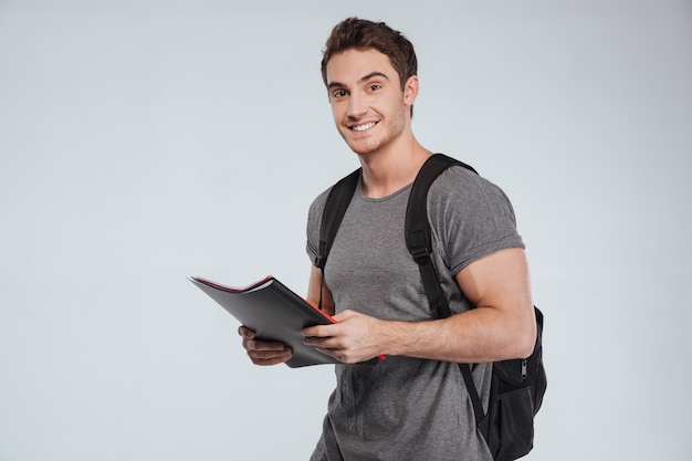 Estudante do sexo masculino sorridente em pé com pastas e mochila em branco