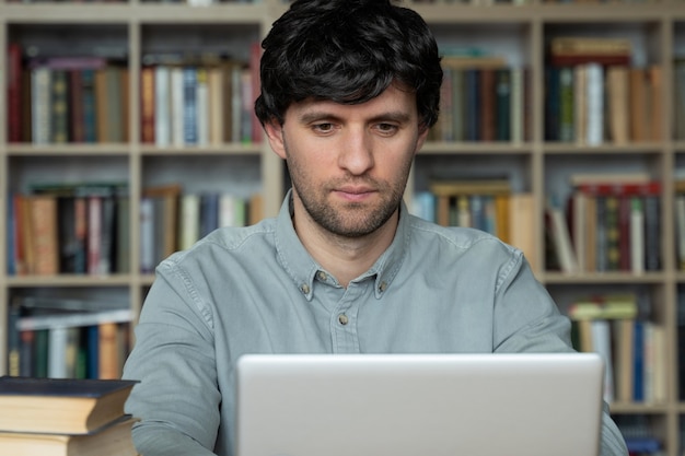 Estudante do sexo masculino usando laptop e estudando na biblioteca da universidade