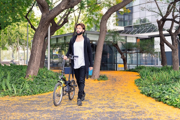 Estudante elegante andando com uma bicicleta no campus