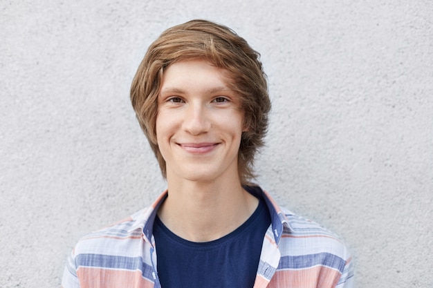 Estudante elegante bonito com penteado na moda vestindo camisa olhando com sorriso na câmera com olhos estreitos escuros e lábios finos