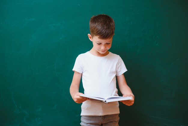 Estudante engraçado perto do conselho escolar verde na sala de aula. Escola primária. De volta à escola.