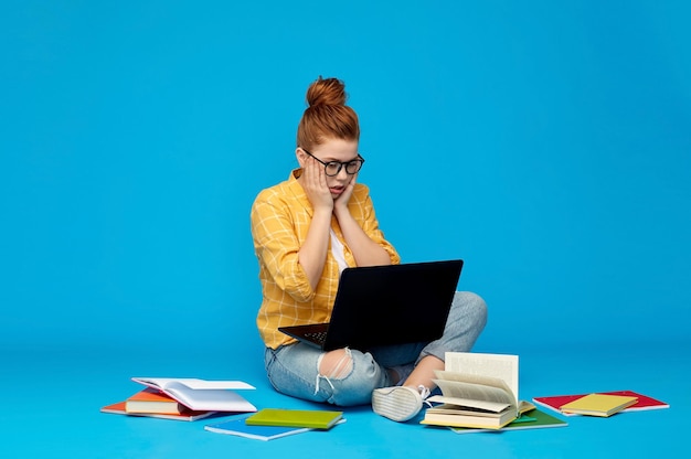 Estudante estressada com laptop e livros.