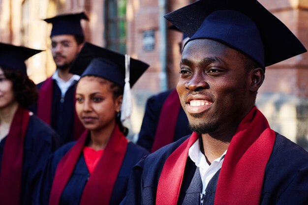 Foto estudante feliz afro-americano de roupão sorrindo enquanto ouve o discurso do professor ao ar livre
