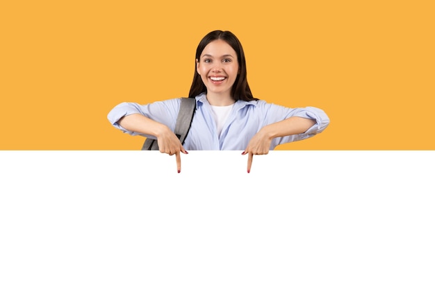 Foto estudante feliz apontando para baixo para uma bandeira em branco