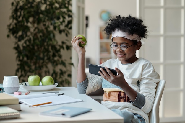 Estudante feliz com maçã verde assistindo vídeo online em smartphone