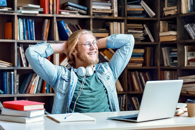 Estudante feliz e relaxado descansando e terminando o trabalho de estudo sentado na biblioteca